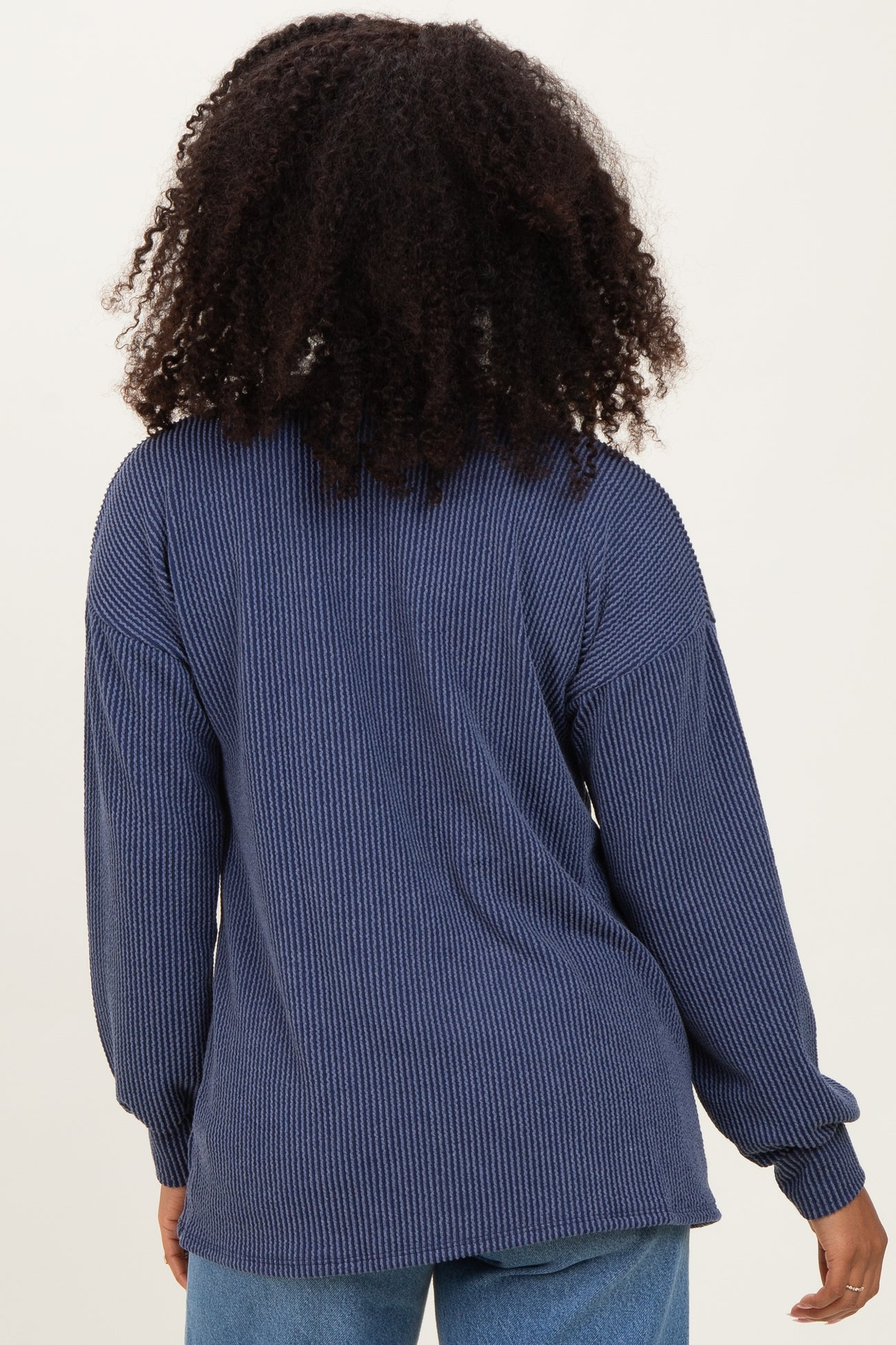 woman wearing a navy blue oversized ribbed long sleeve top, seen from the back with curly hair visible