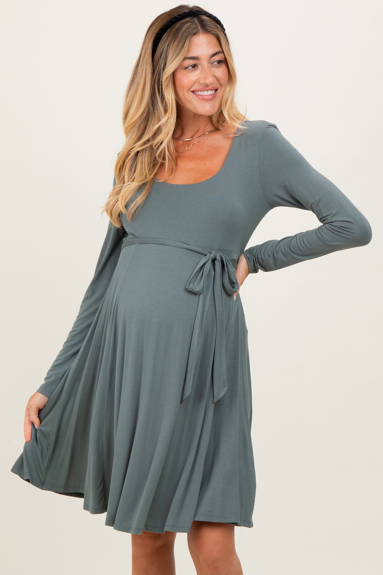 woman wearing a sage green long sleeve maternity dress with a tie at the waist and a visible baby bump