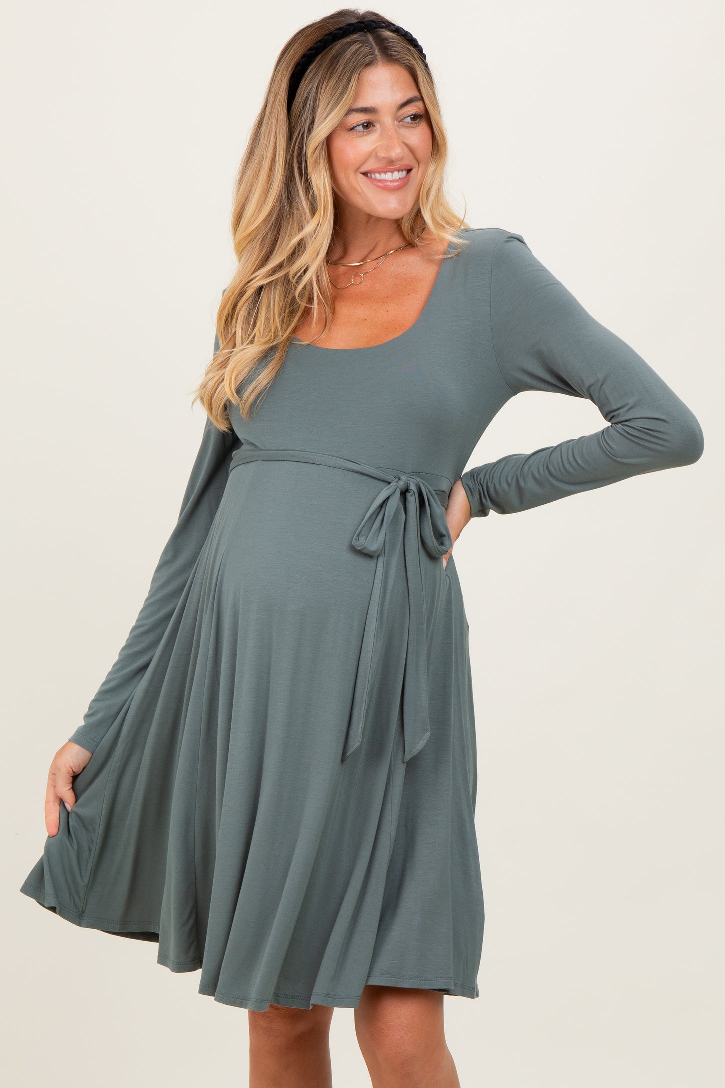 woman wearing a sage green long sleeve maternity dress with a tie at the waist and a visible baby bump