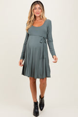 woman wearing a teal long sleeve maternity dress with a tie waist and a visible baby bump