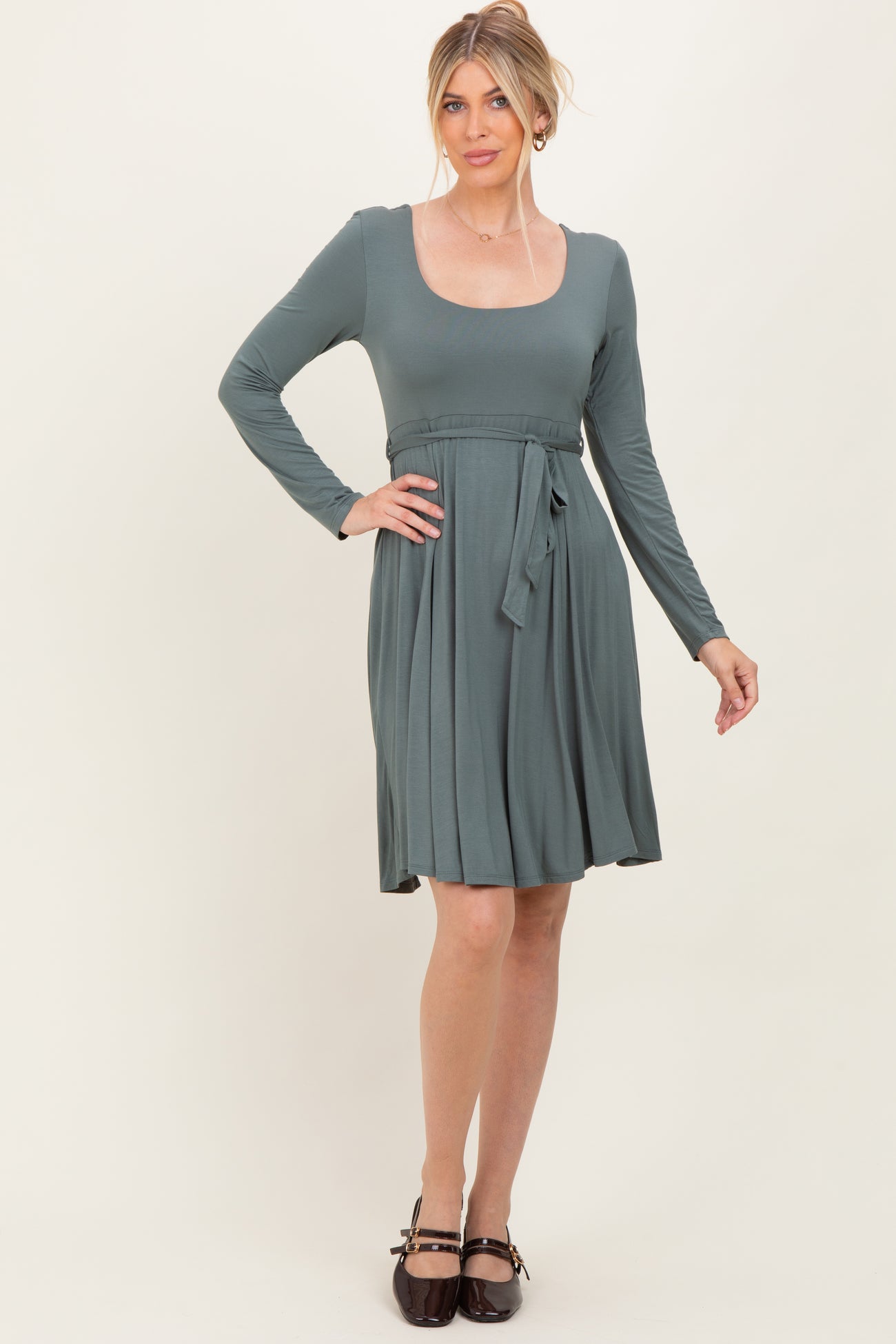 woman wearing a forest green long sleeve dress with a tie waist and pleated skirt.