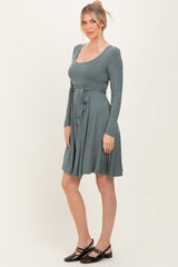 woman wearing a teal long sleeve wrap dress with a tie belt and a flared skirt