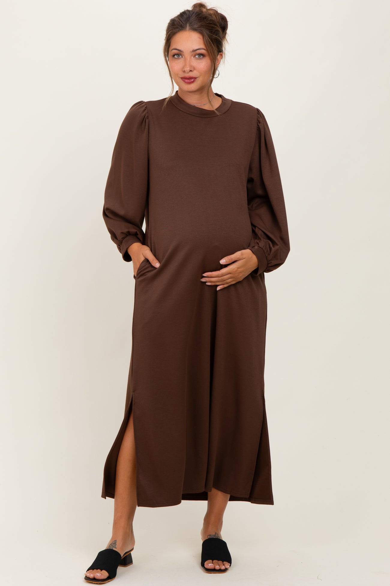 woman wearing a brown long sleeve maternity dress with side slits and pockets, holding her baby bump
