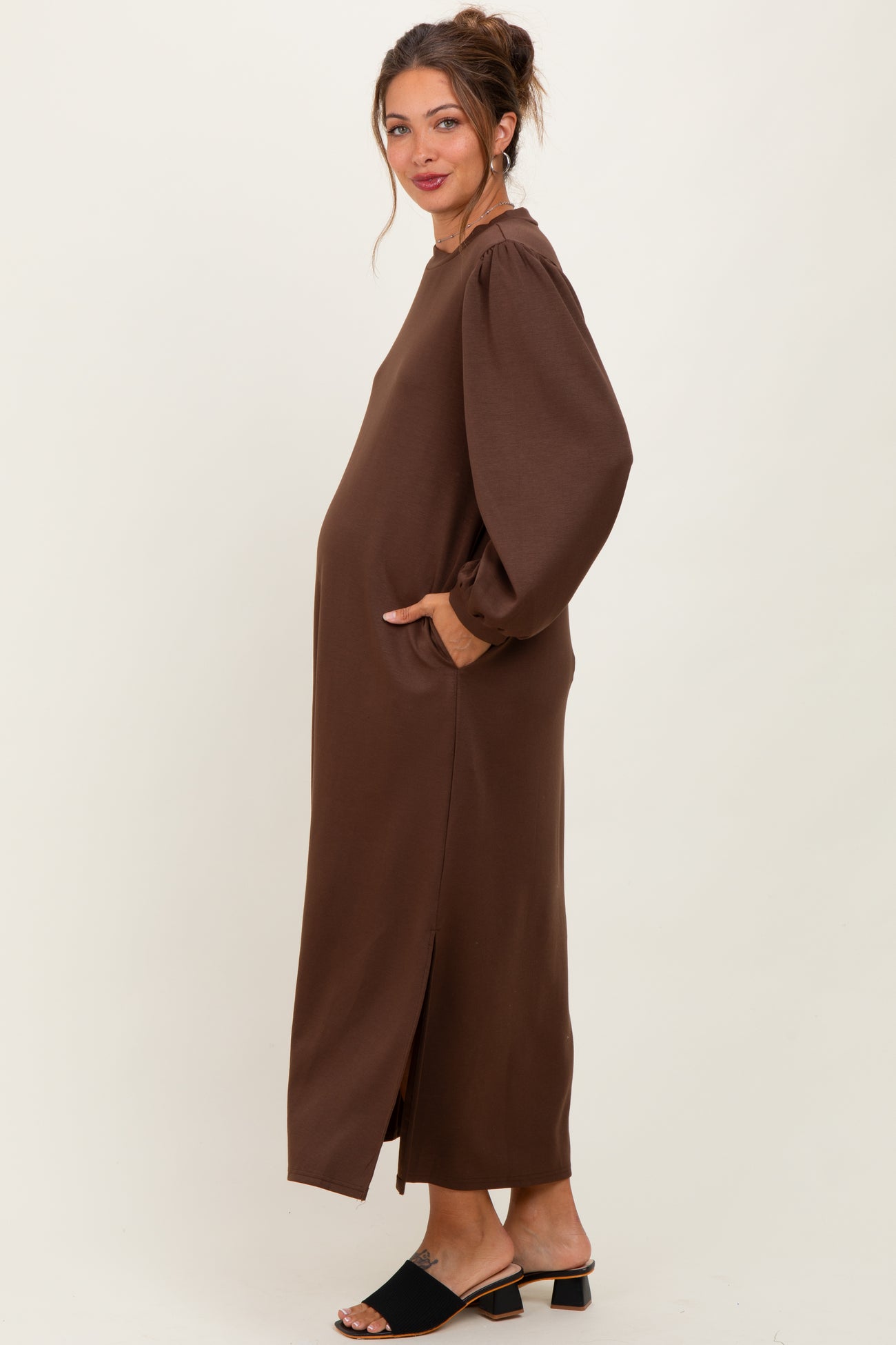 woman wearing a brown long sleeve maternity dress with side slits and pockets, showcasing her baby bump