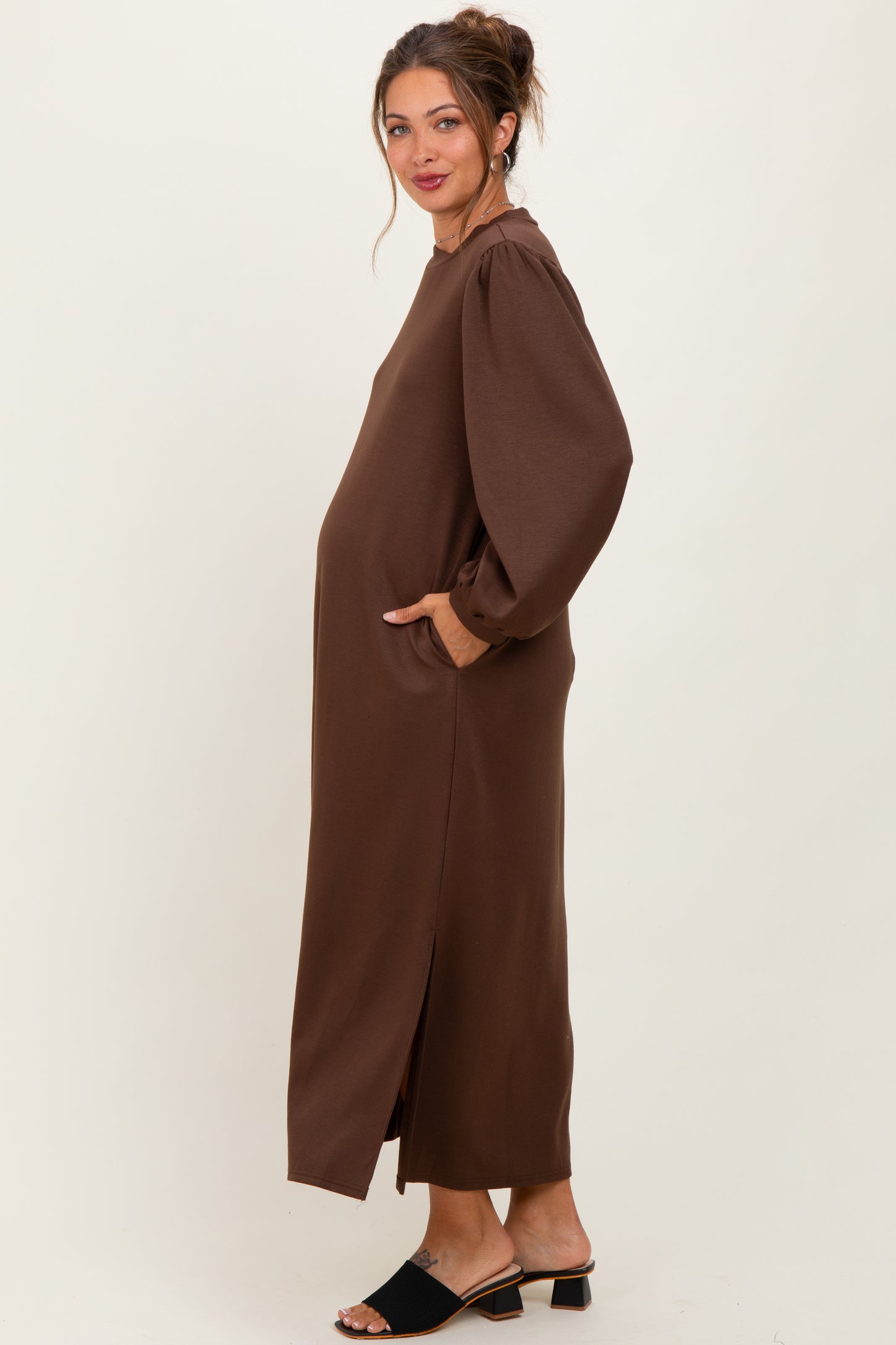 woman wearing a brown long sleeve maternity dress with side slits and pockets, showcasing her baby bump
