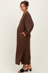 woman wearing a brown long sleeve maternity dress with side slits and pockets, showcasing her baby bump