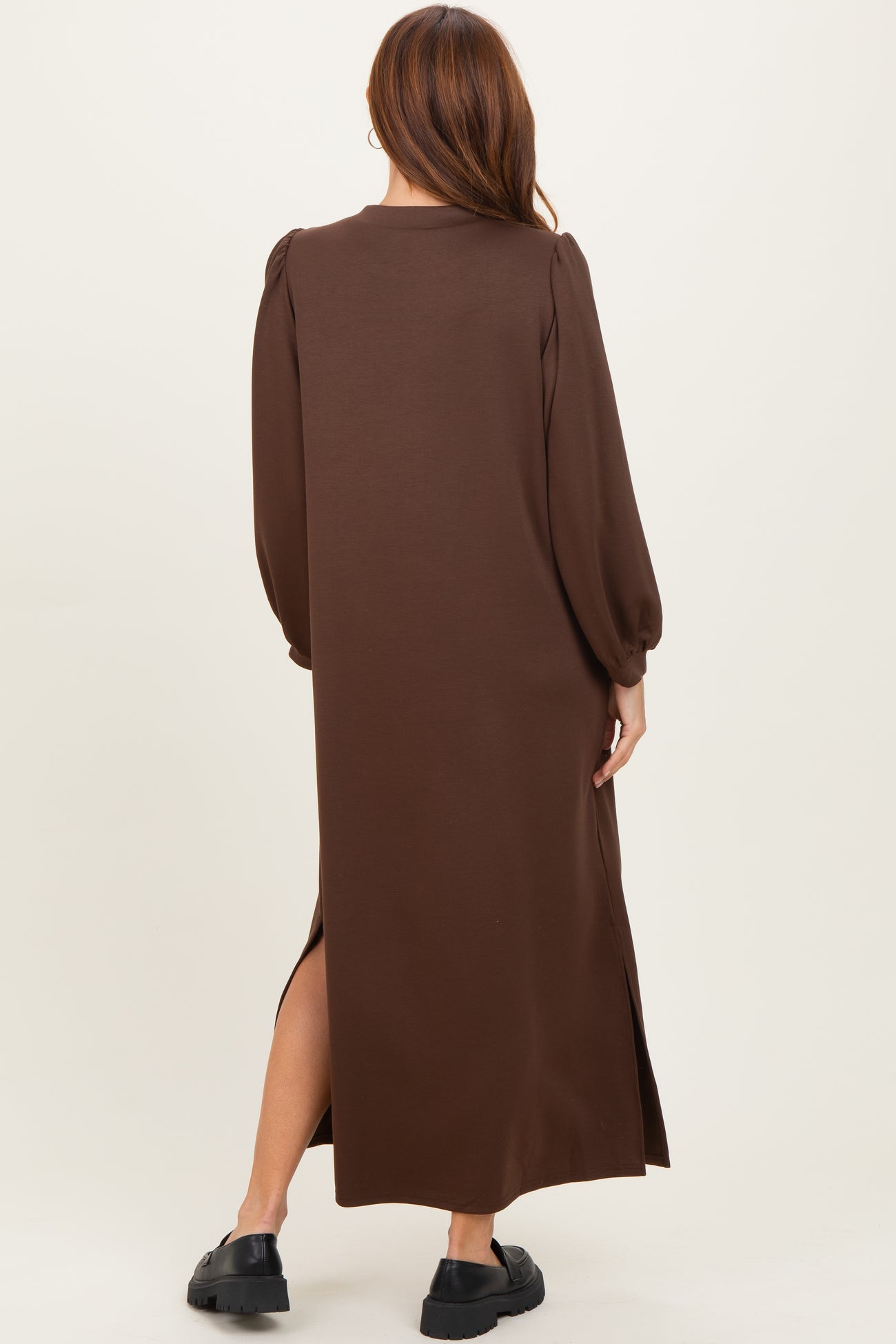 woman wearing a brown long sleeve maxi dress with puff sleeves and side slits, viewed from the back