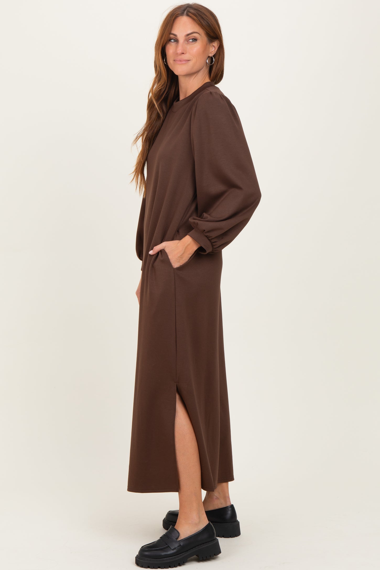 woman wearing a brown long sleeve maxi dress with pockets and side slits, styled casually with black footwear