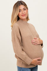 woman wearing a tan sweater and jeans, cradling her baby bump, showcasing maternity wear