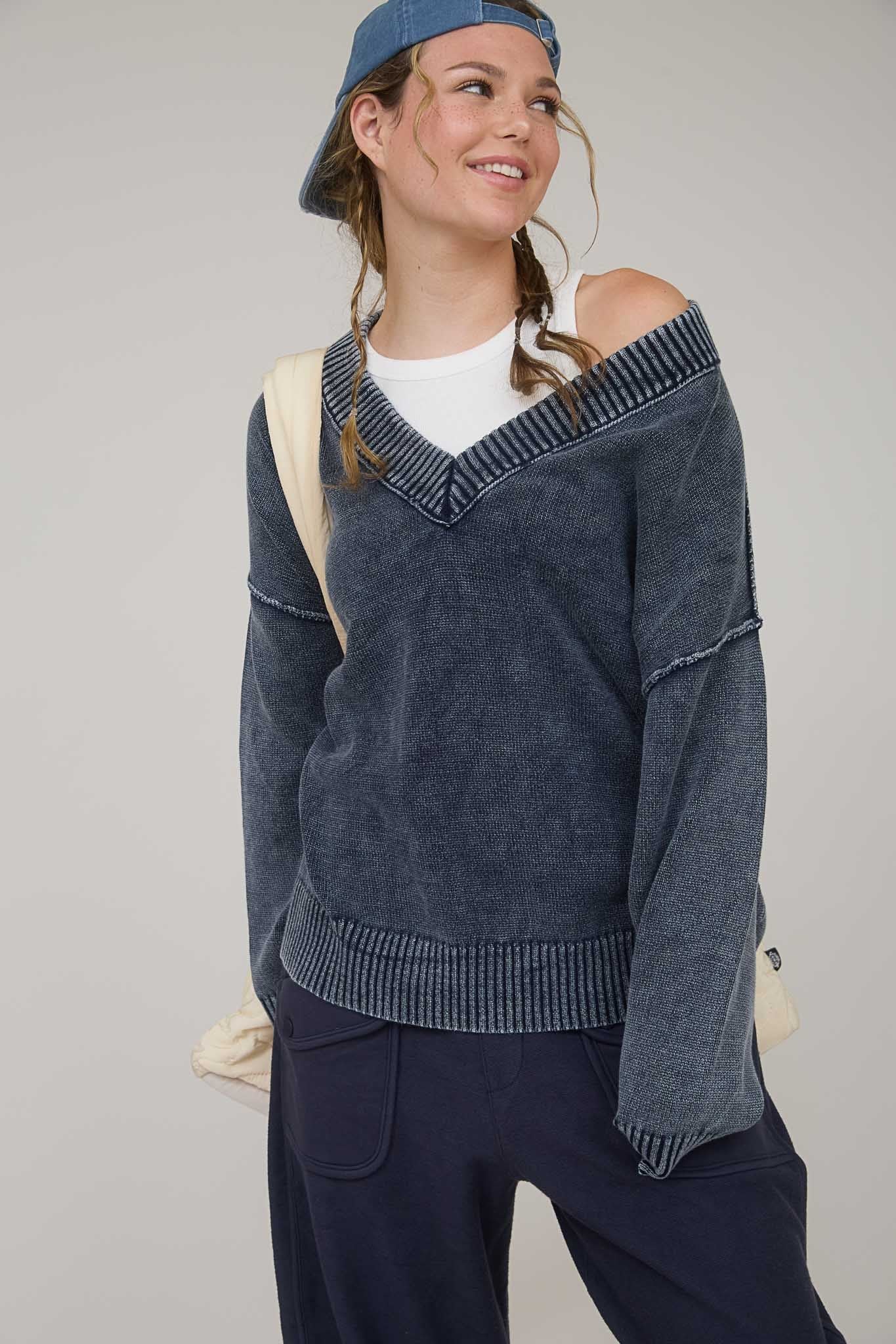 woman wearing a dark blue off-shoulder sweater with ribbed details and a casual cap