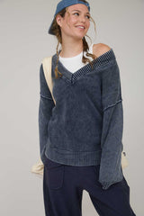 woman wearing a dark blue off-shoulder sweater with ribbed details and a casual cap
