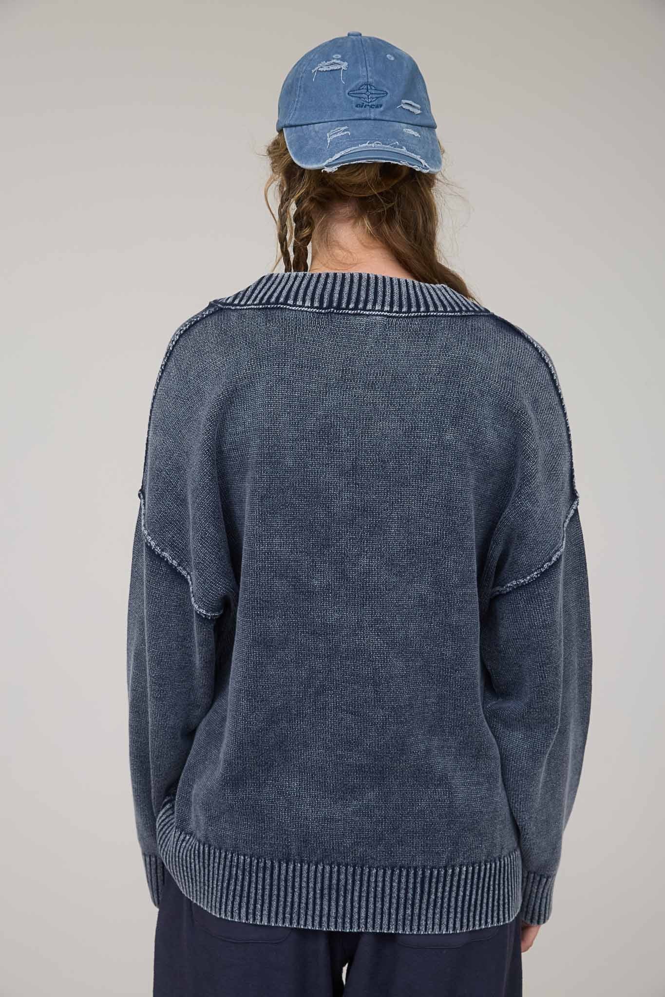 woman wearing a navy blue oversized sweater with a ribbed neckline and back details, styled with a casual cap