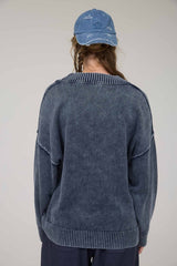 woman wearing a navy blue oversized sweater with a ribbed neckline and back details, styled with a casual cap