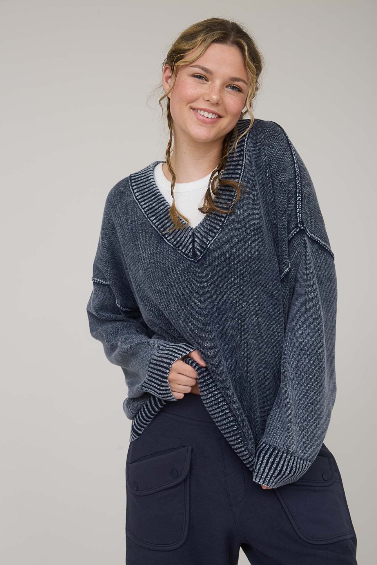 woman wearing a navy oversized sweater with a v-neck and striped detailing, paired with dark pants