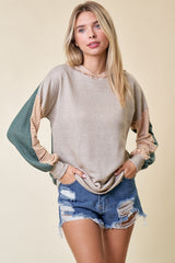 woman wearing a tan and green colorblocked long sleeve hoodie with striped detailing and distressed denim shorts