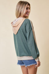 woman wearing a green and beige color block hoodie with a striped hood and denim shorts