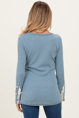 woman wearing a blue maternity top with lace detail and button accents on the sleeves, showing her back