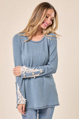 woman wearing a light blue ribbed top with lace details on sleeves and button accents standing against a neutral background