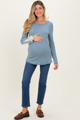 woman wearing a blue ribbed long sleeve maternity top with decorative sleeves and holding her baby bump