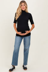 woman wearing a black short sleeve maternity top and blue jeans, cradling her baby bump
