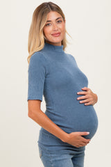 woman wearing a blue ribbed maternity top and gently cradling her baby bump