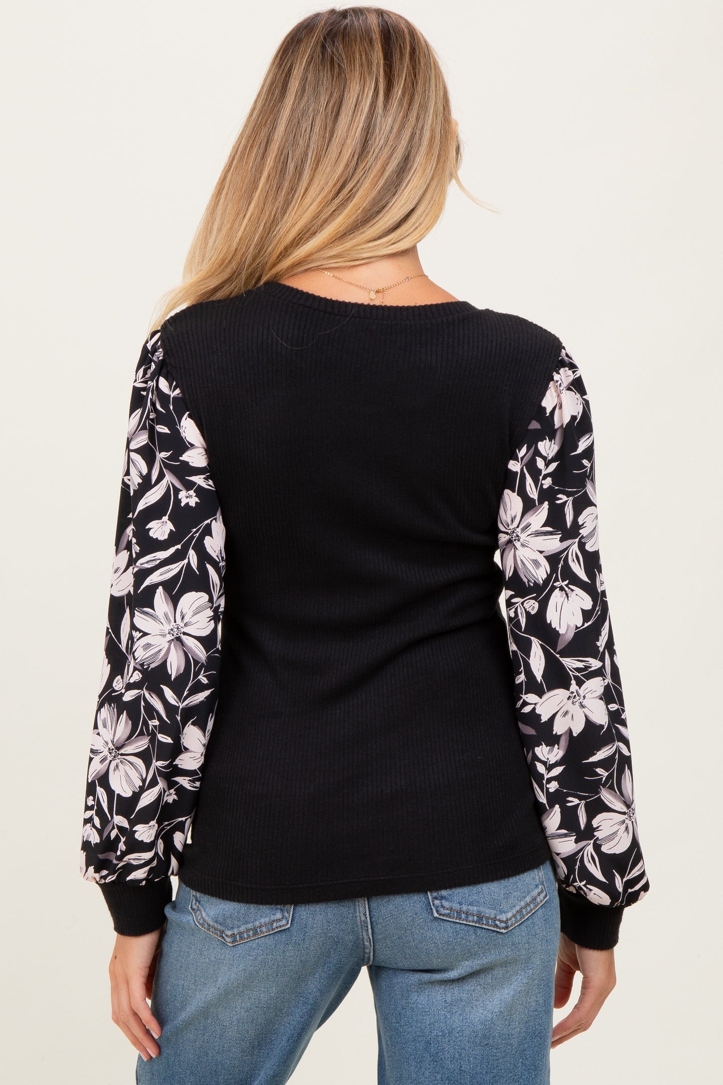 woman wearing a black maternity top featuring floral print long sleeves and a fitted bodice