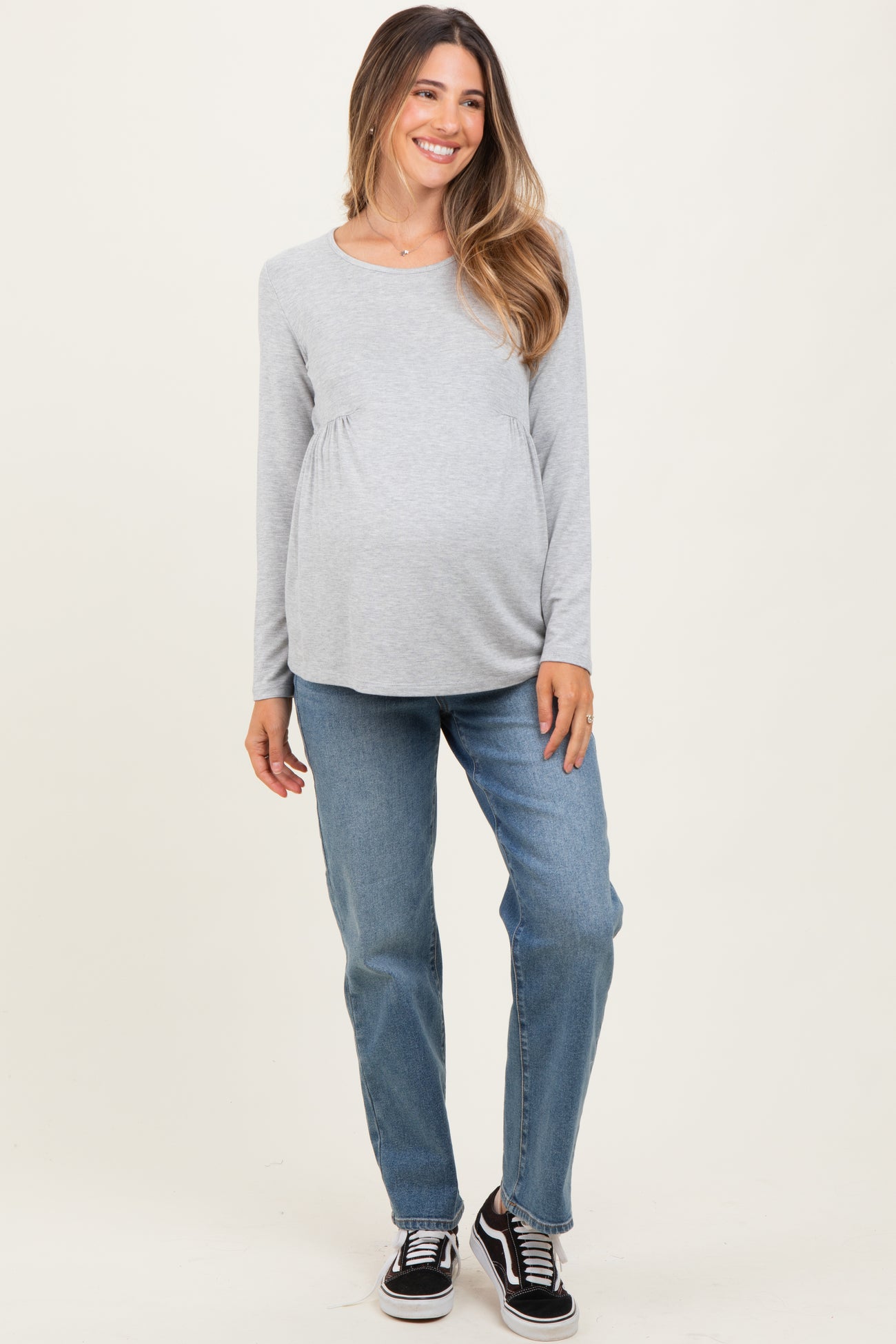 woman wearing a gray long sleeve maternity top and blue jeans, displaying her baby bump