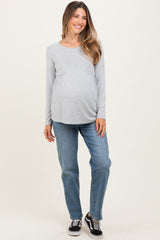 woman wearing a gray long sleeve maternity top and blue jeans, displaying her baby bump