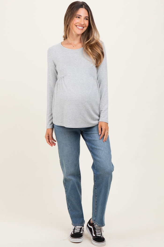 woman wearing a gray long sleeve maternity top and blue jeans, displaying her baby bump