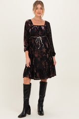 woman wearing a black floral maternity dress with long sleeves and a cinched waist, paired with knee-high black boots