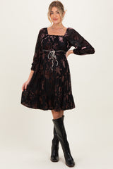 woman wearing a black floral maternity dress with long sleeves and a cinched waist, styled with knee-high black boots