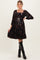 woman wearing a black floral maternity dress with long sleeves and a cinched waist, styled with knee-high black boots