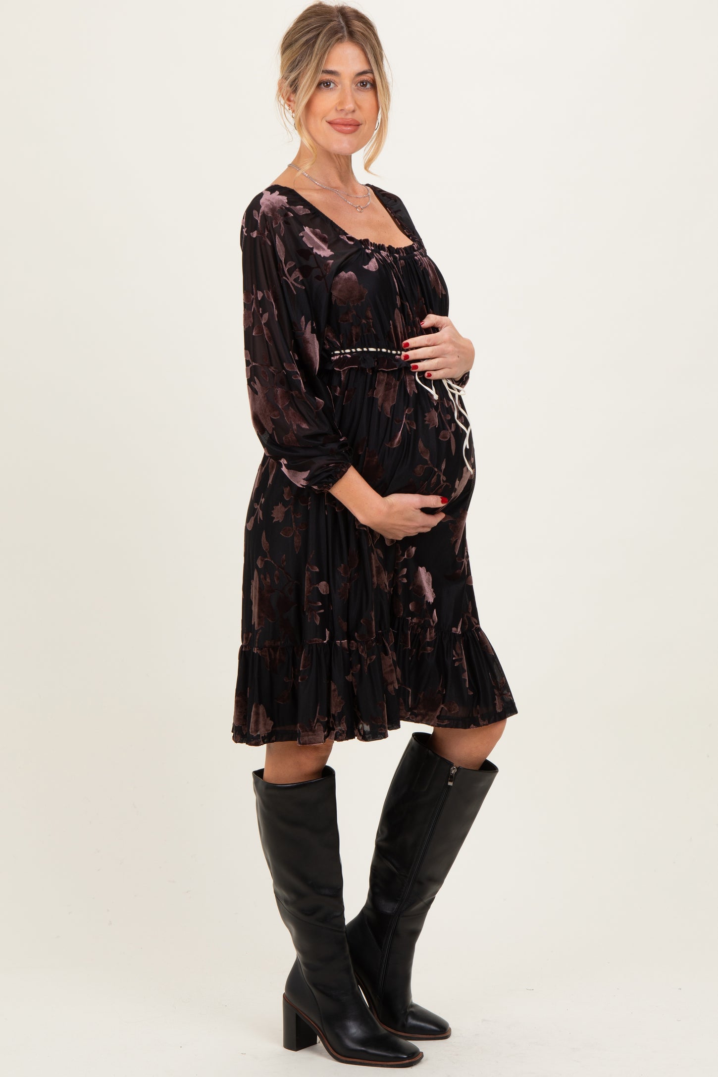 woman wearing a black floral maternity dress with a ruffled hem and holding her baby bump