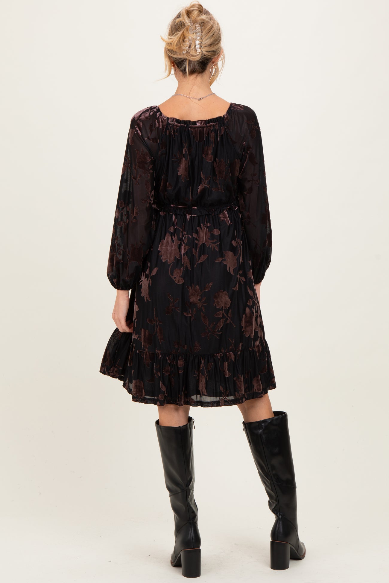 woman wearing a black floral print maternity dress with long sleeves and a ruffled hem, highlighted by a baby bump