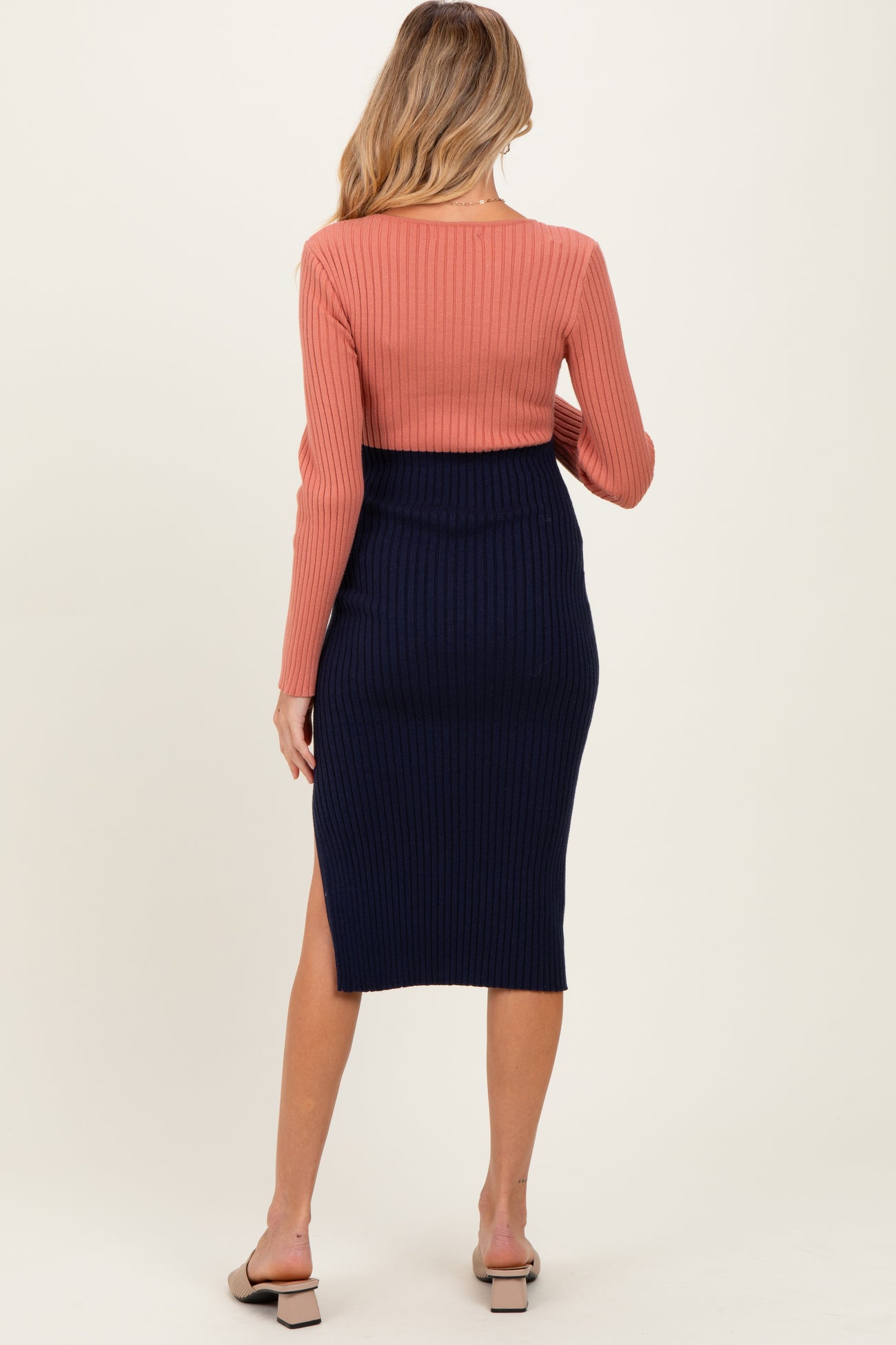 woman wearing a rust-colored ribbed maternity top and navy ribbed maternity skirt with a side slit, view from the back