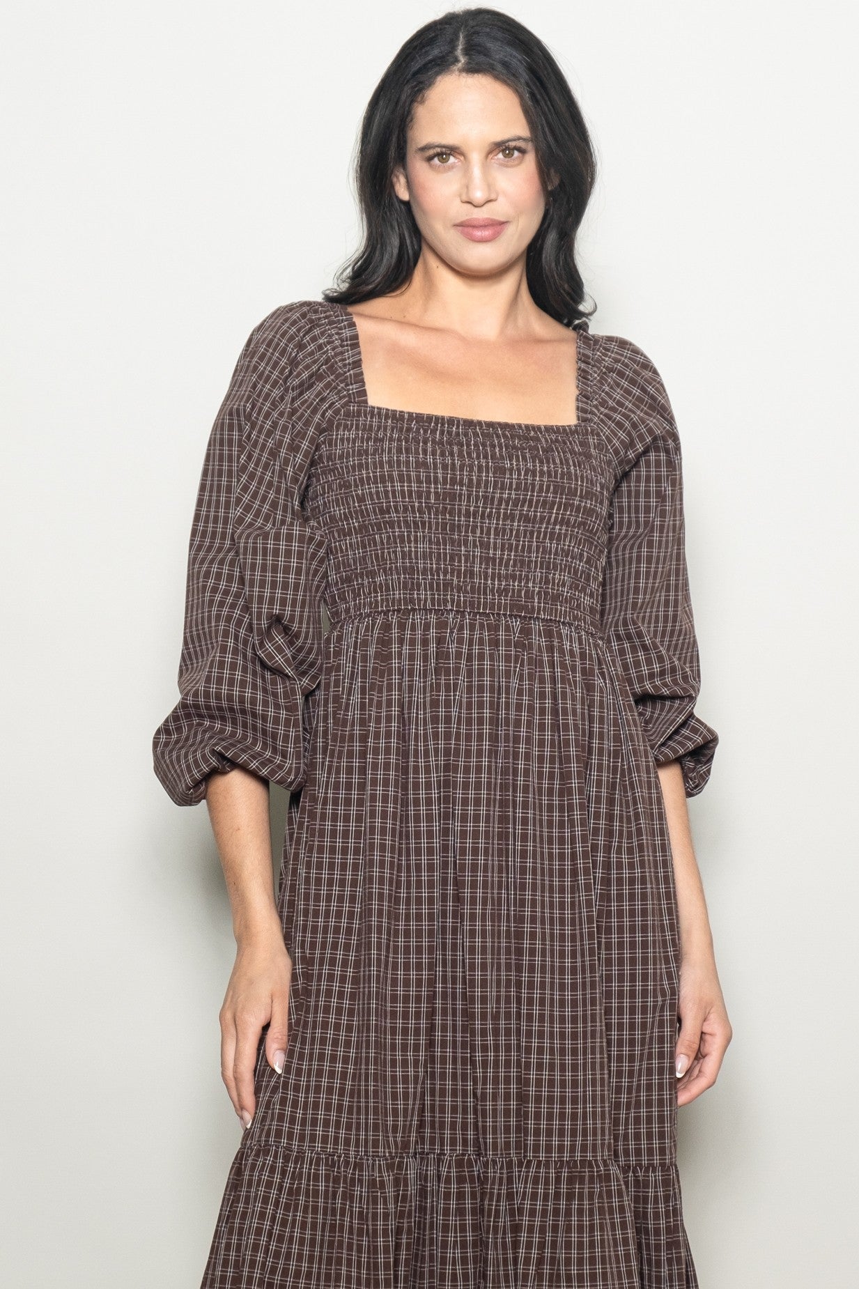 woman wearing a brown checkered puff sleeve dress with a square neckline and tiered skirt
