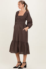 woman wearing a brown checkered maternity dress with a square neckline and ruffle hem, holding her baby bump
