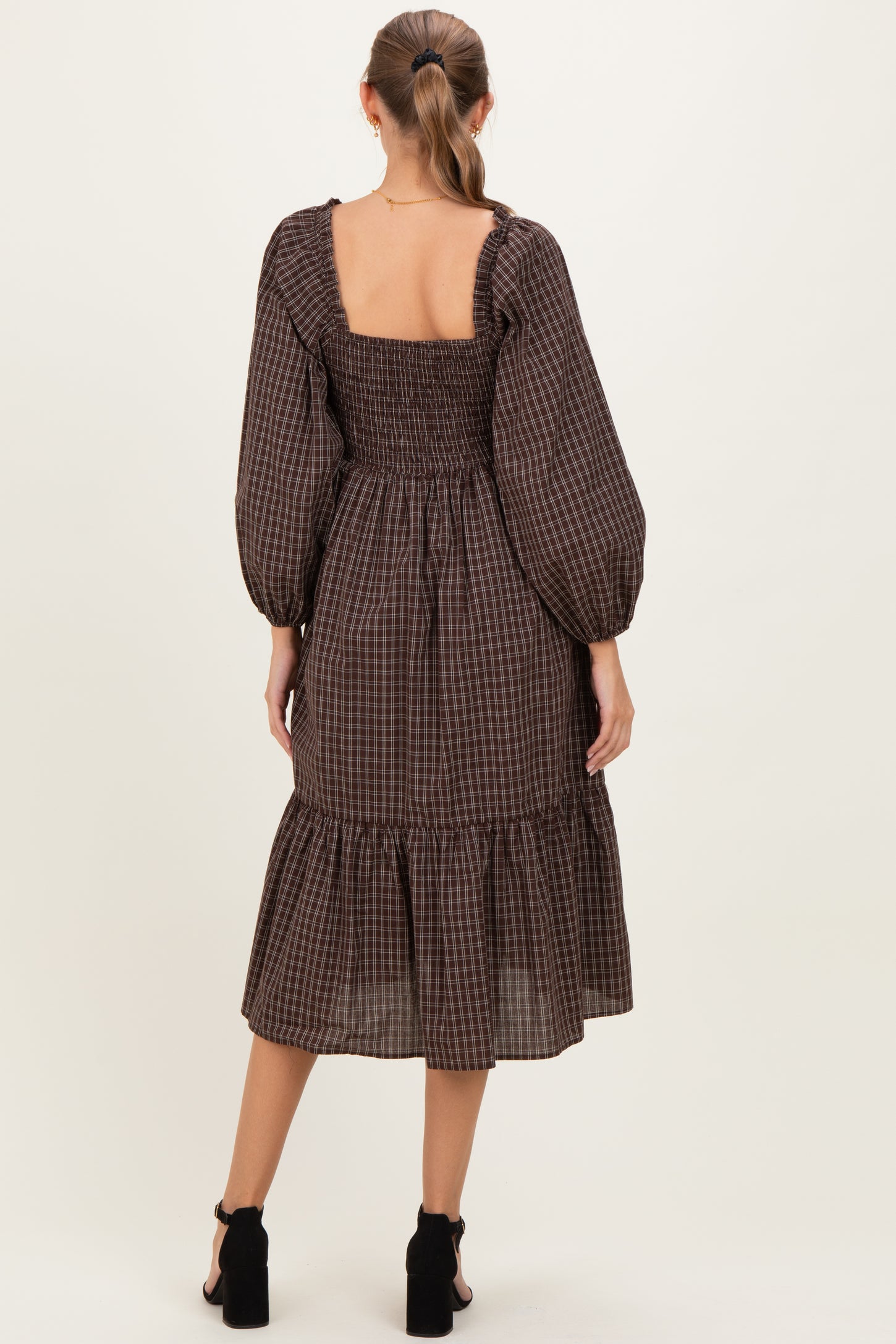 woman wearing a brown checkered smocked maternity dress with long puff sleeves and a tiered hem, seen from the back