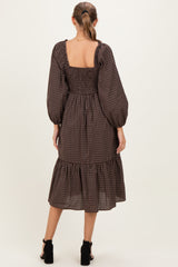 woman wearing a brown checkered smocked maternity dress with long puff sleeves and a tiered hem, seen from the back