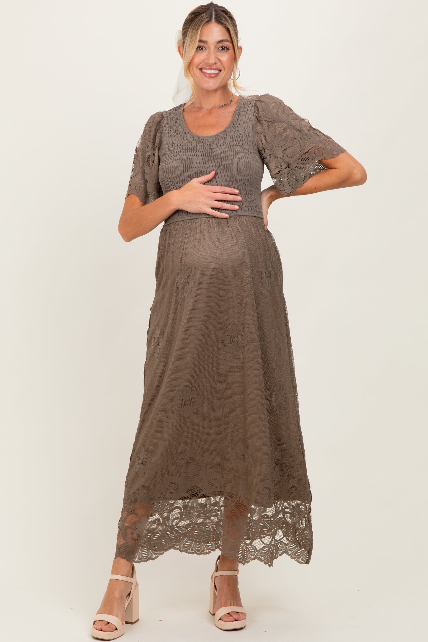 woman wearing a brown maternity dress with floral lace details, holding her baby bump