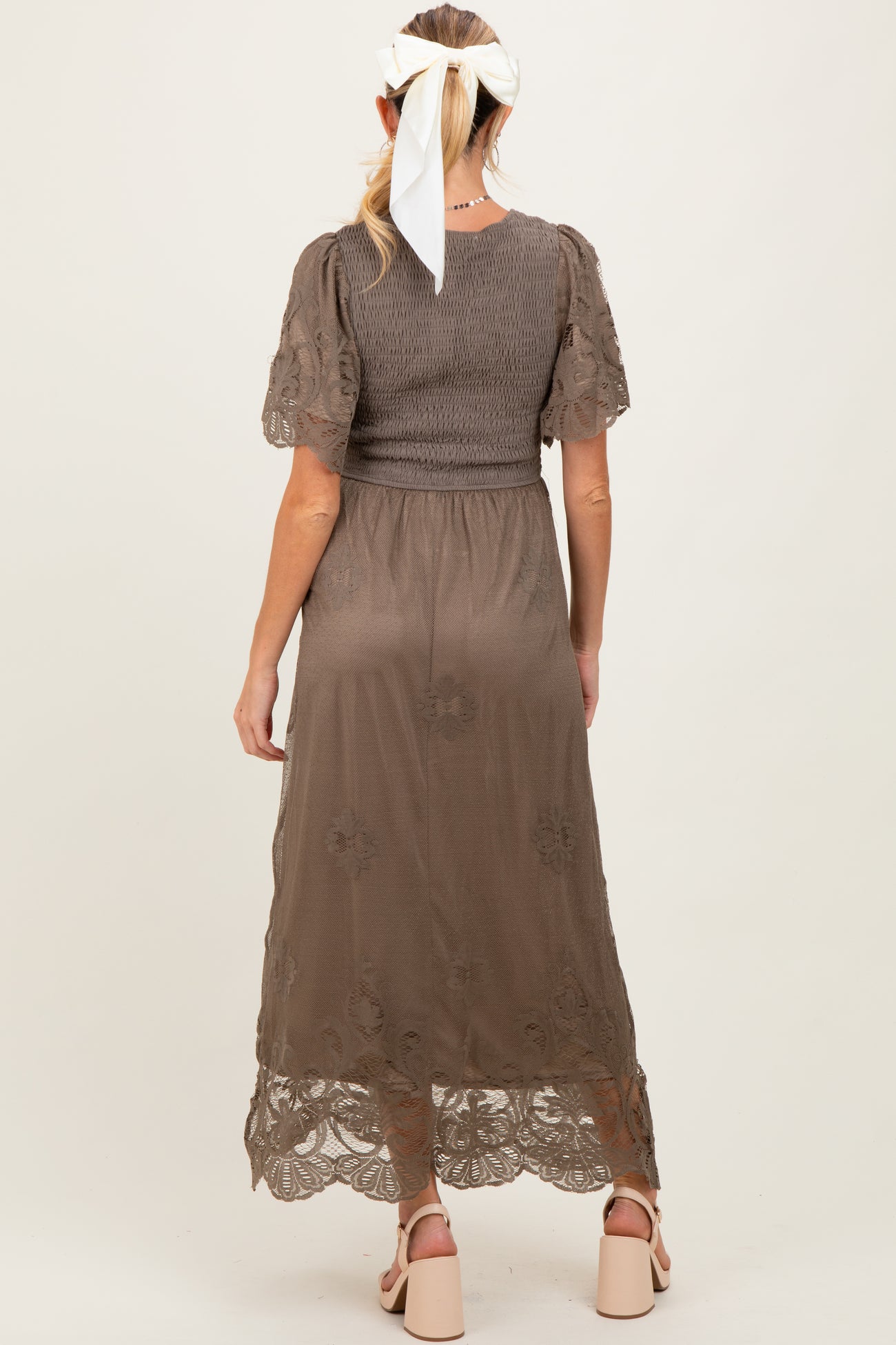 woman wearing a brown maternity dress with a smocked bodice and floral lace hem, seen from the back