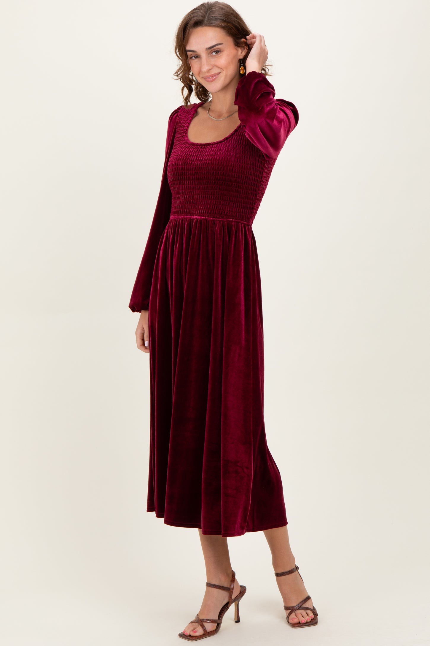 woman wearing a burgundy velvet midi dress with a smocked bodice and long sleeves, posing in a relaxed stance