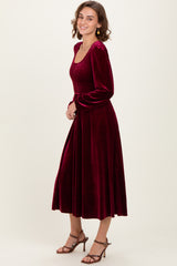 woman wearing a burgundy velvet long sleeve dress with a smocked bodice and a flowing skirt, smiling and posing