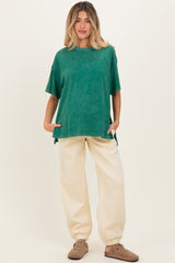 woman wearing a green oversized maternity top with short sleeves and cream-colored maternity jogger pants