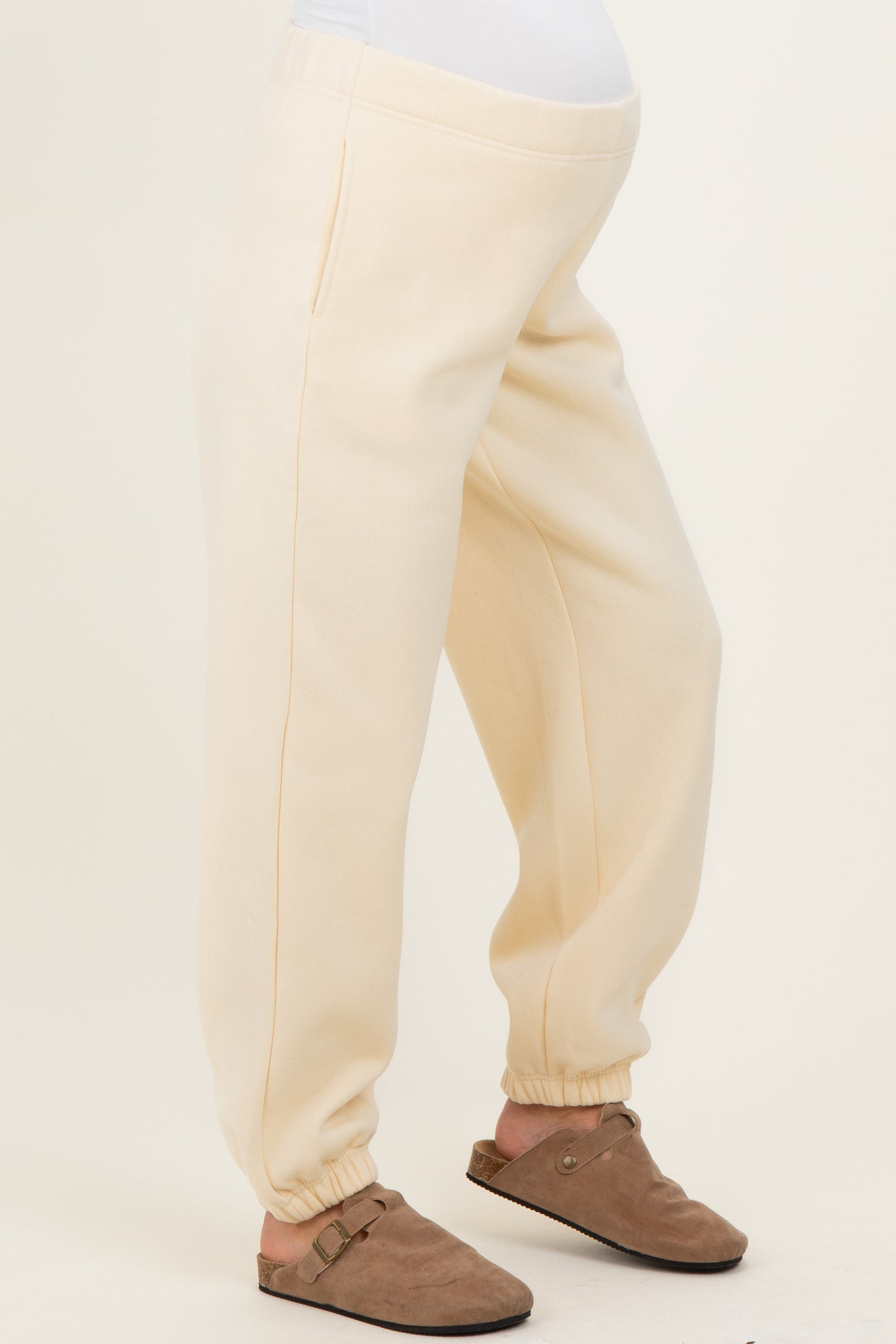 woman wearing cream-colored maternity joggers with elastic cuffs and a comfortable waistband, baby bump visible