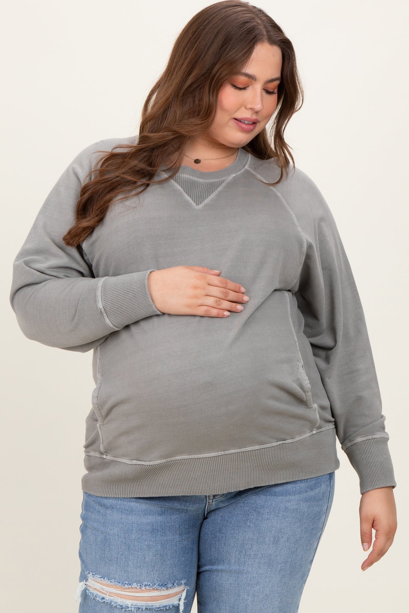 woman wearing a gray maternity plus sweatshirt with side ruching and holding her baby bump