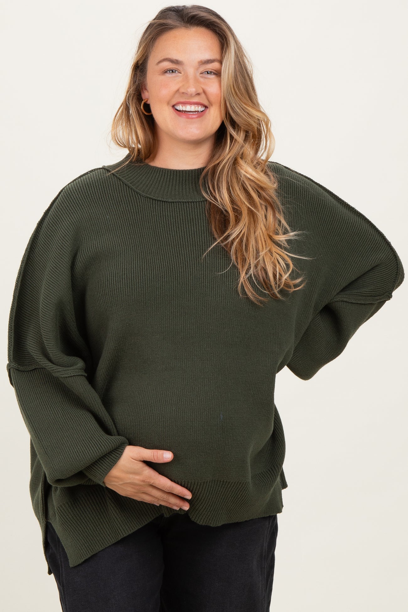 woman wearing a dark green oversized maternity sweater and holding her baby bump