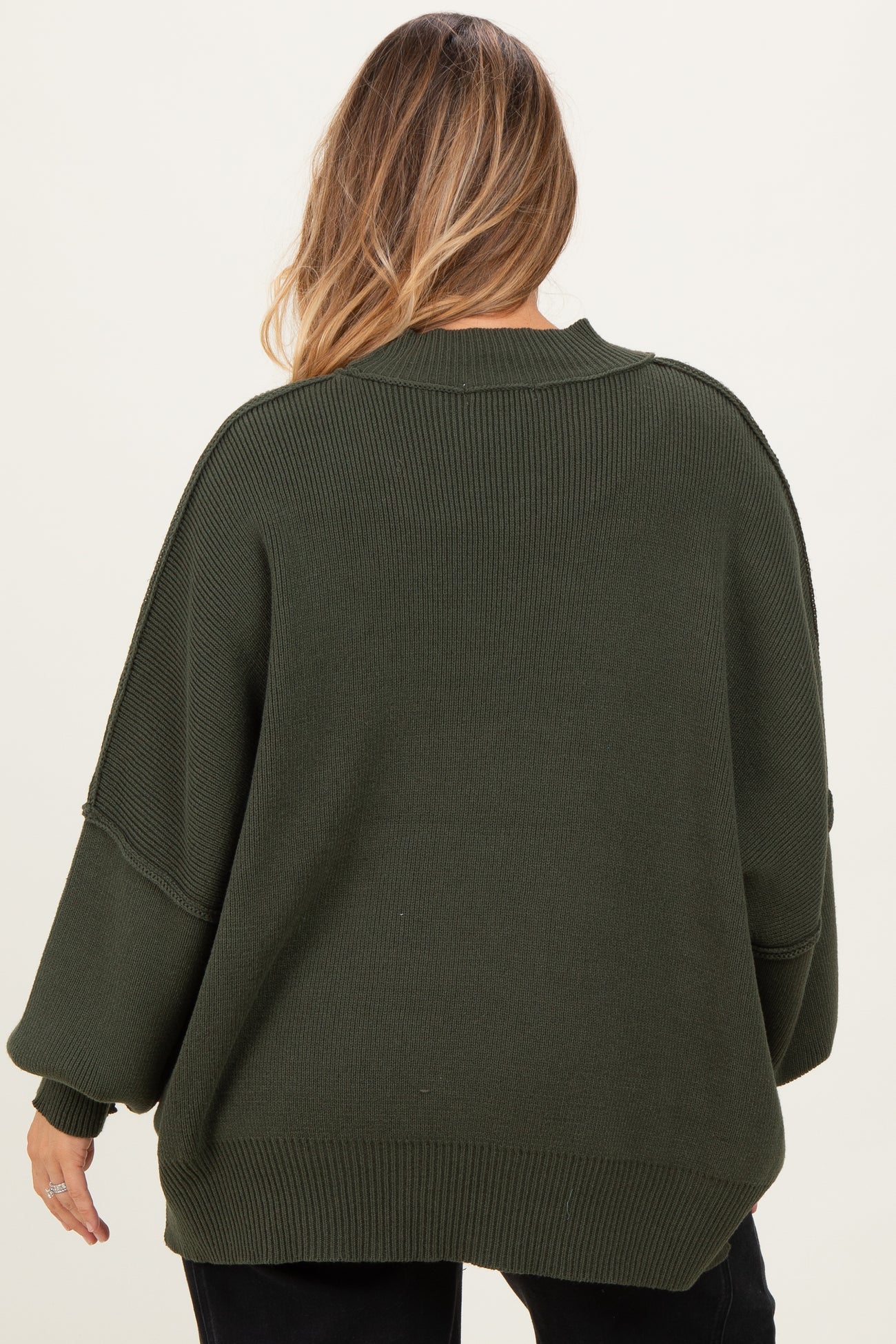 woman wearing an olive green oversized maternity sweater with wide sleeves, seen from the back