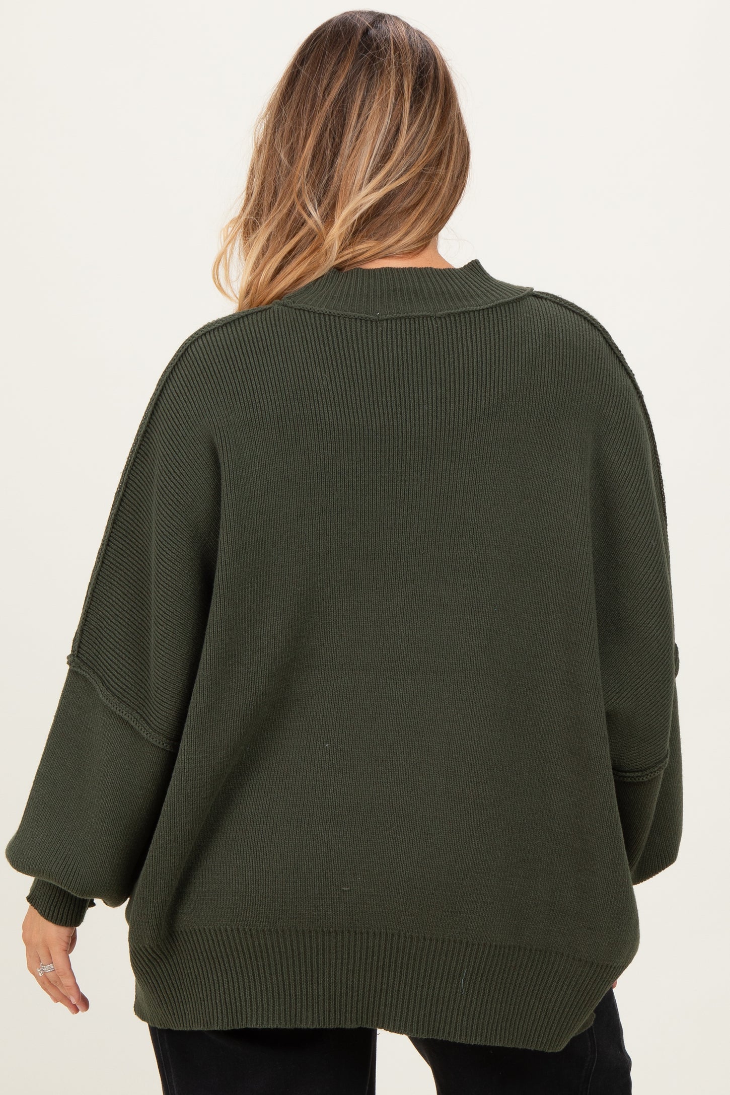 woman wearing an olive green oversized maternity sweater with wide sleeves, seen from the back