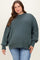 woman wearing a dark green oversized maternity plus sweater with a high neckline and long sleeves, paired with blue jeans